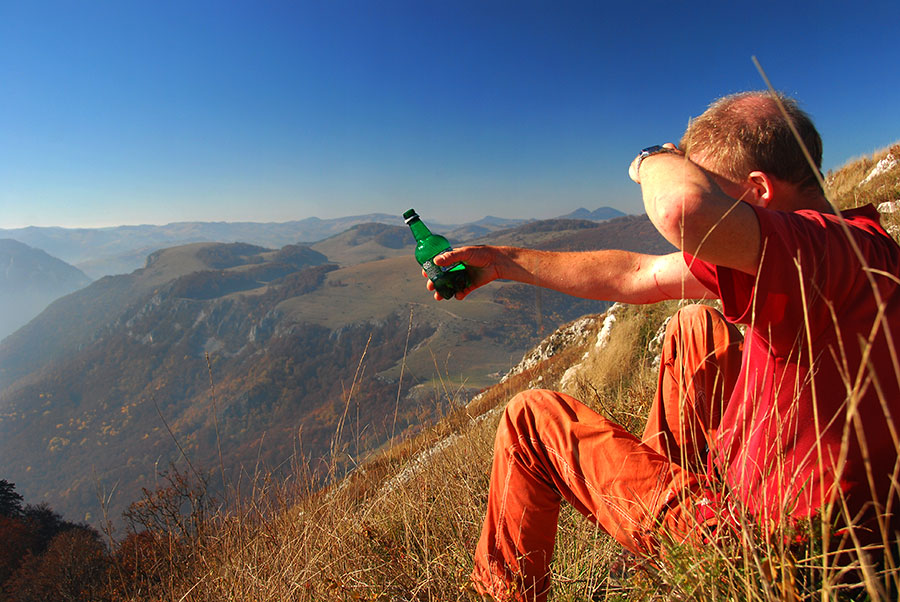 Mann sitzt auf einem Berg mit einer Flasche Bier in der Hand