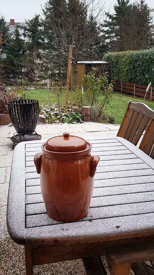 Tonkrug steht auf einem leicht verschneiten Tisch auf der Veranda von Gudruns Garten