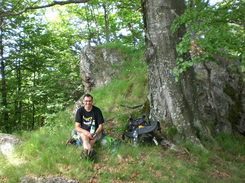 Wanderer sitzt auf seinem Rucksack unter einem Baum und macht Pause