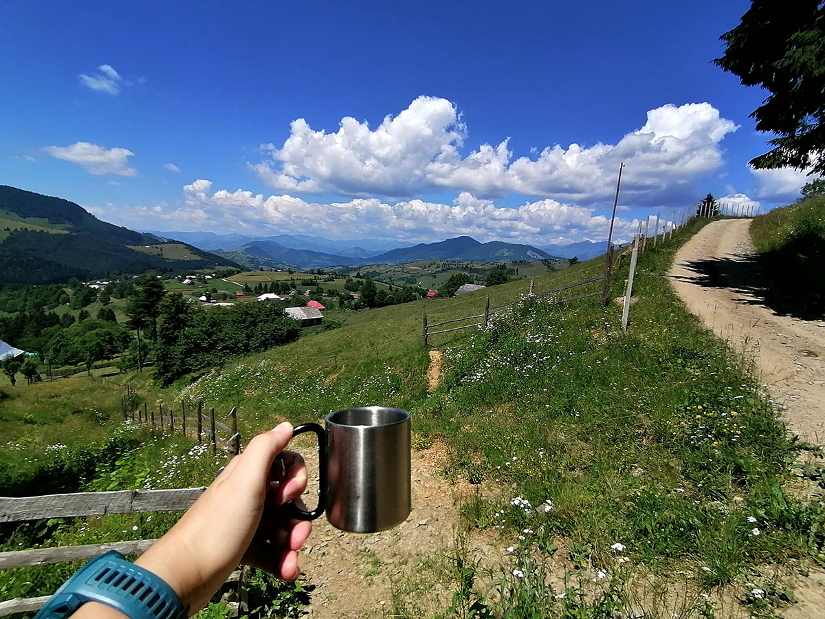 Hand mit eine Kaffeetasse vor schöner Berglandschaft