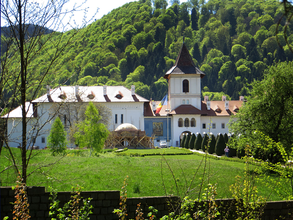 Klosteranlage mit grüner Wiese davor und gehisster rumänischer Flagge