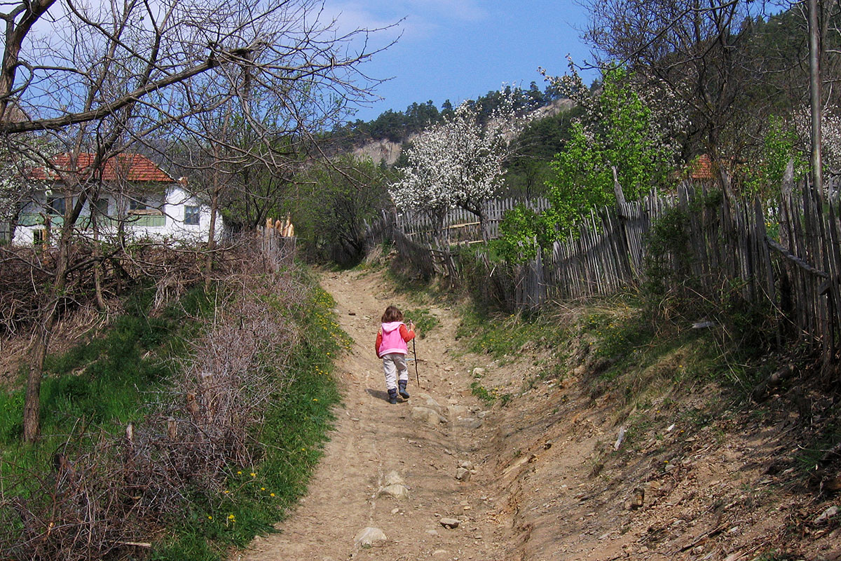 Mädchen läuft mit einem Wanderstock einen unbefestigten Weg im Dorf hoch