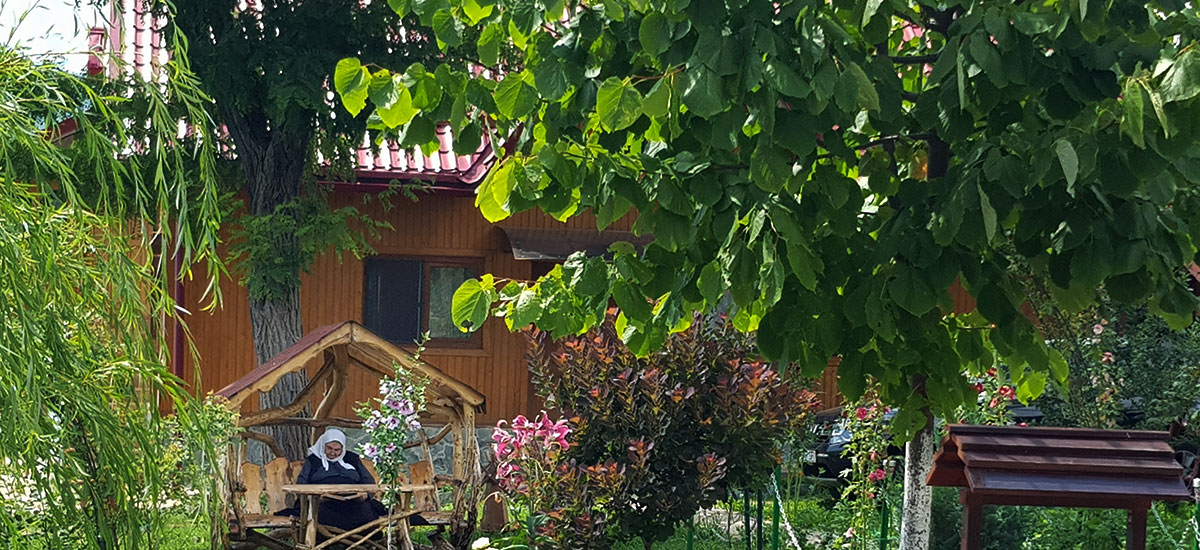 Frau mit Kopftuch sitzt auf einer überdachten Bank im Garten