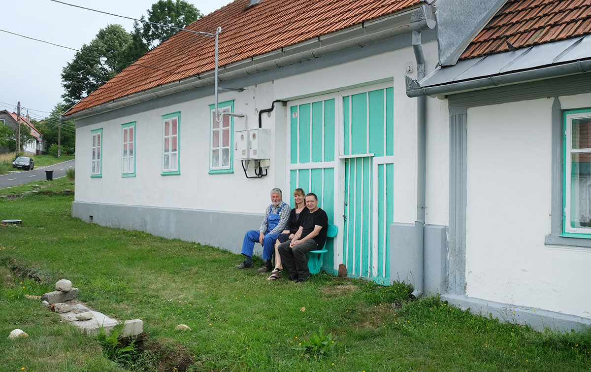 Drei Menschen auf einer Bank vor einem Haus