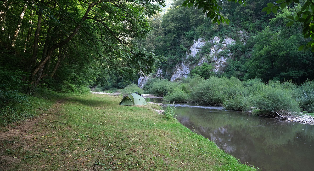 Zelt steht am Flussrand auf einer Wiese