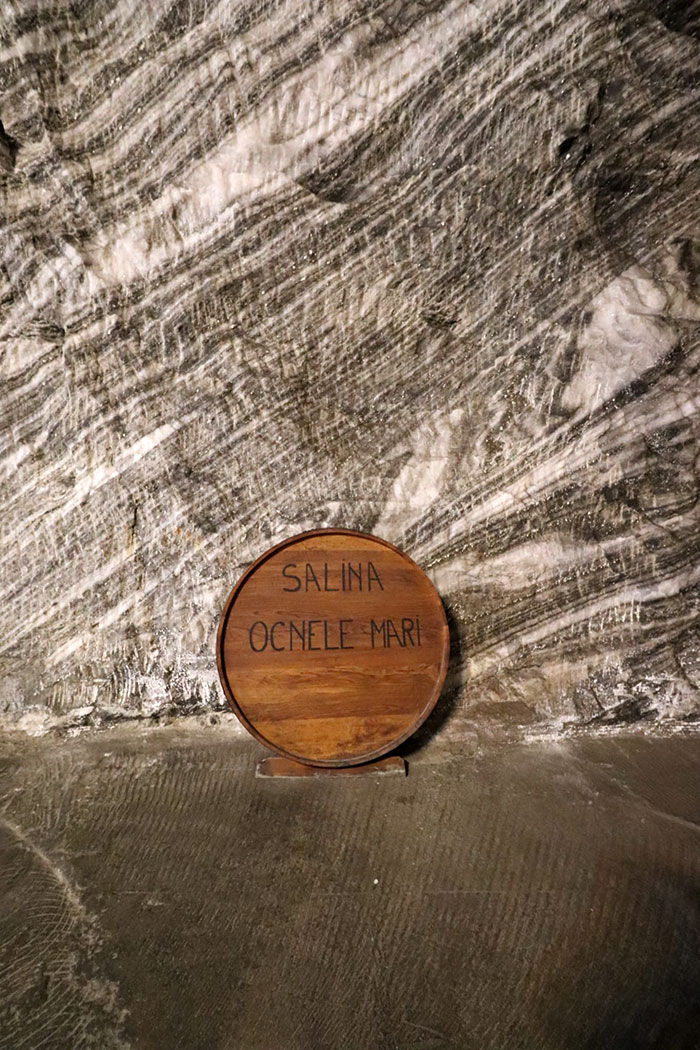 rundes Holzschild mit Aufschrift Salina Ocnele Mari vor Salzwand in Höhle
