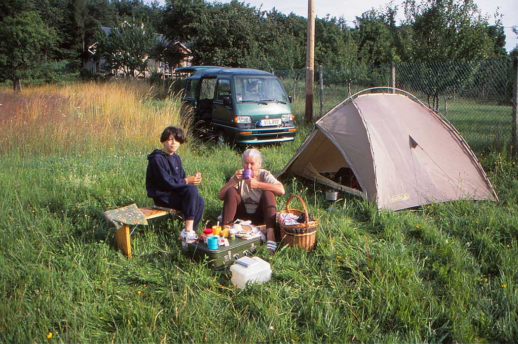 Menschen essen auf einer Wiese vor einem Zelt